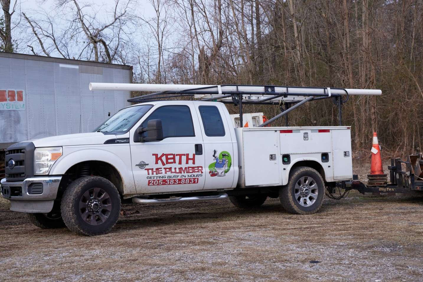 A white Keith The Plumber Ford service truck with a utility bed, carrying PVC pipes on a roof rack