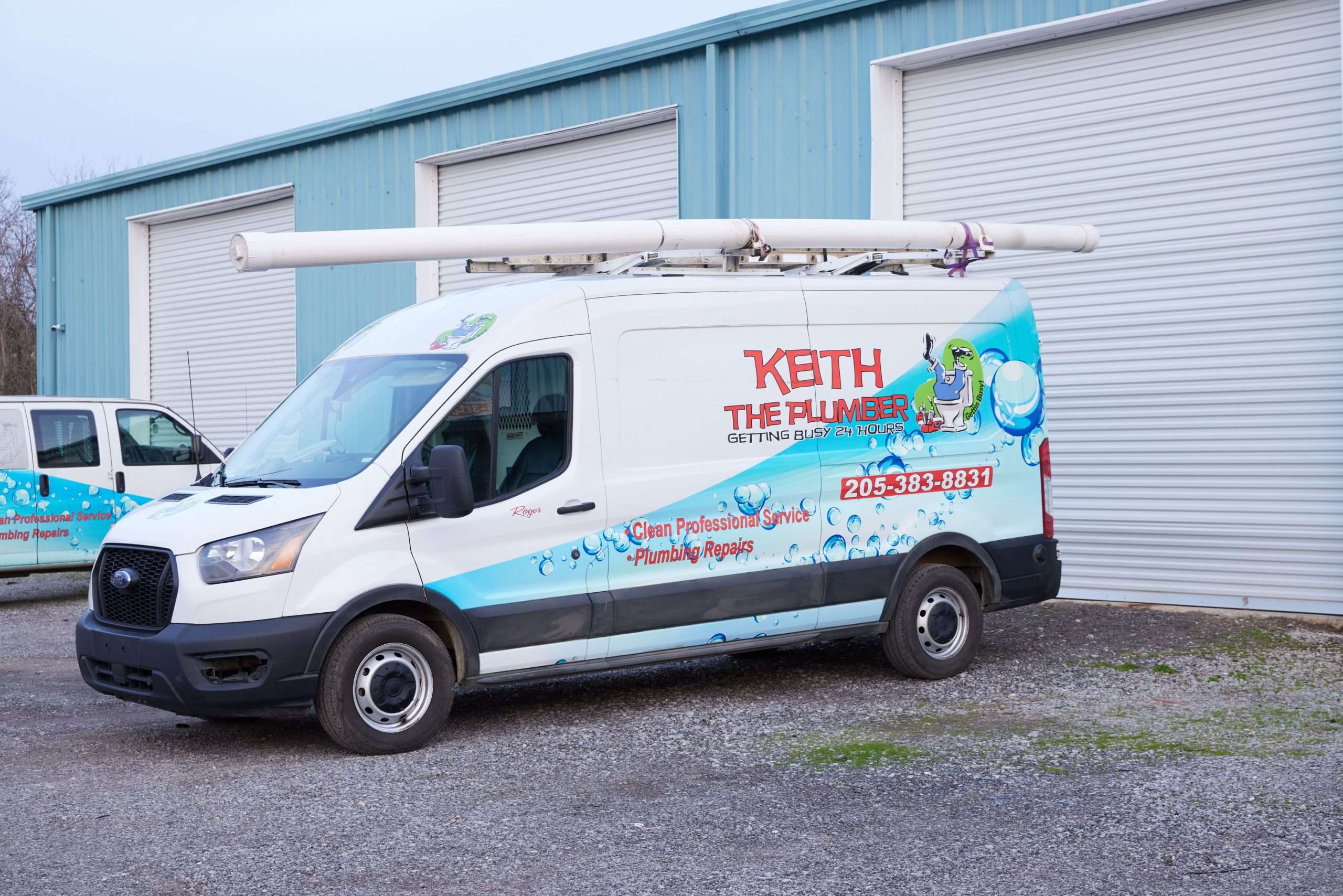 A white Keith The Plumber Ford Transit service van parked in front of a blue warehouse